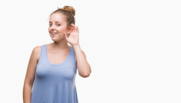 Jeune femme blonde souriante avec la main sur l'oreille en écoutant une rumeur ou des commérages. Concept de surdité
. - Photo, image