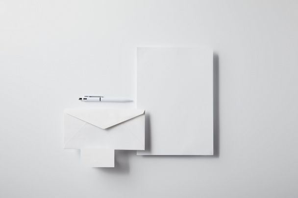 top view of layered envelope with pen, blank paper and business card on white surface for mockup - Photo, Image