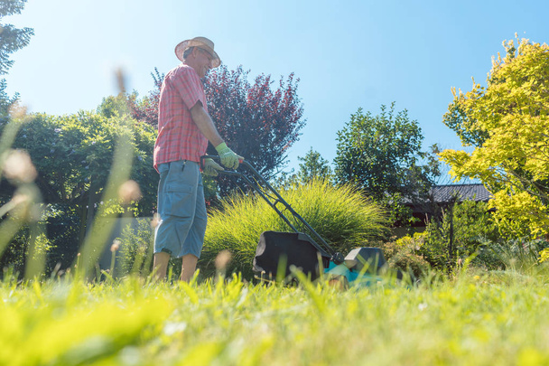 Активный пожилой человек улыбается при помощи газонокосилки
 - Фото, изображение