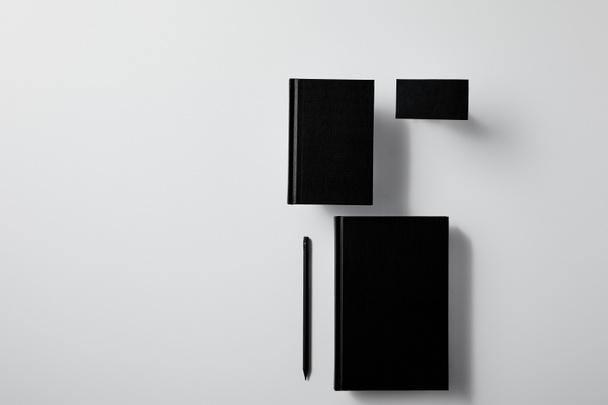 top view of arranged black notebooks with business card and pencil on white surface for mockup - Photo, Image