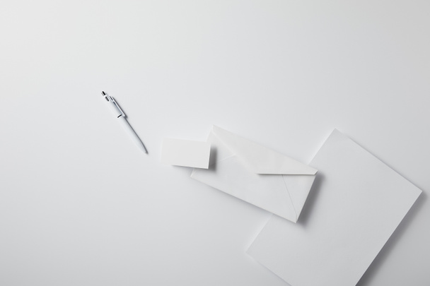 kalem, boş kağıt ve kartvizit ile düzenlenmiş zarf üstten görünüm mockup için beyaz yüzeyi - Fotoğraf, Görsel