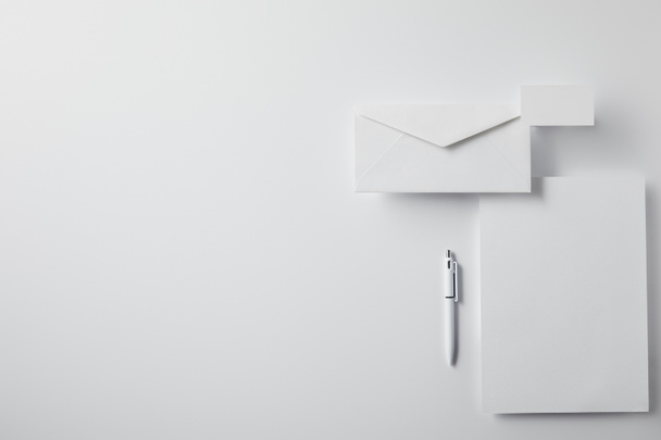 top view of layered envelope with pen, blank paper and business card on white surface for mockup - Zdjęcie, obraz