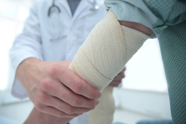 Orthopedist applying bandage onto patients hand in clinic - Photo, Image