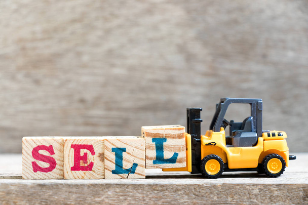 Spielzeug Gabelstapler halten Buchstabe Block l in Wort verkaufen auf Holz Hintergrund - Foto, Bild