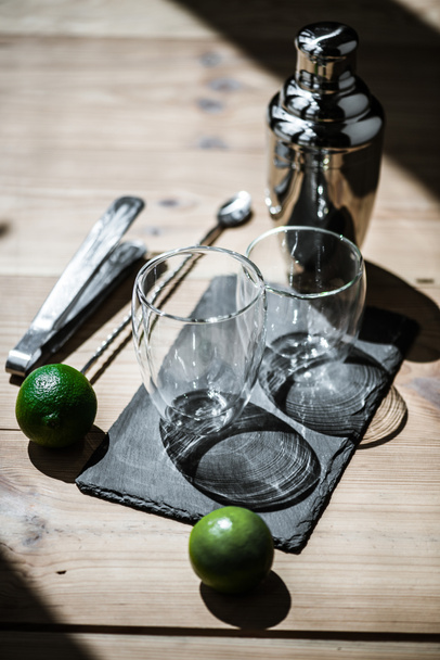 vista de cerca de limas frescas, vasos vacíos, pinzas y agitador en la mesa de madera
  - Foto, Imagen