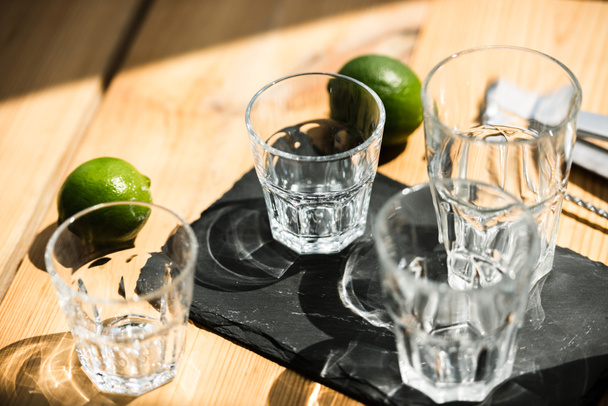 close-up view of empty glasses, tongs and fresh limes on wooden table  - Foto, afbeelding