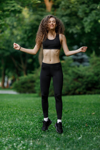 beautiful curly woman doing exercises warming up before running in summer park. - Fotó, kép