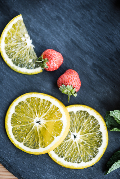 top view of fresh sliced lemon and ripe strawberries on slate board - Photo, Image