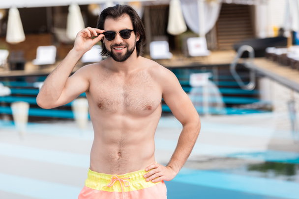handsome bearded man in sunglasses posing at swimming pool  - Photo, Image