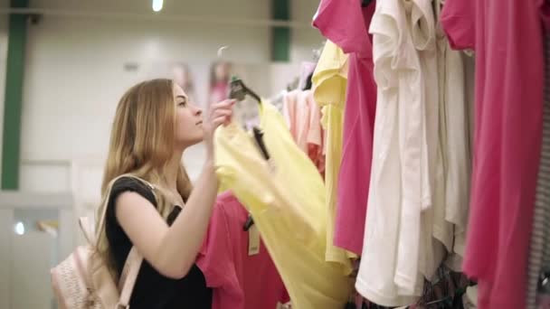 Dziewczynka bierze t-shirt z wieszaka w sklepie i wprowadzenie innych na stojaku - Materiał filmowy, wideo