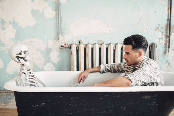 Homme d'affaires en faillite assis dans la baignoire contre le squelette humain, concept d'homme suicidaire. Problème dans les affaires, dépression
 - Photo, image