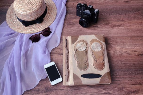 fotoalbum s plácat, fotoaparát, telefon, parero, slaměný klobouk a sluneční brýle, na dřevěné pozadí - Fotografie, Obrázek