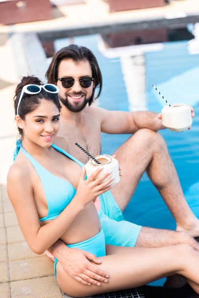 pareja joven en gafas de sol con cocteles de coco relajante en la piscina
  - Foto, Imagen