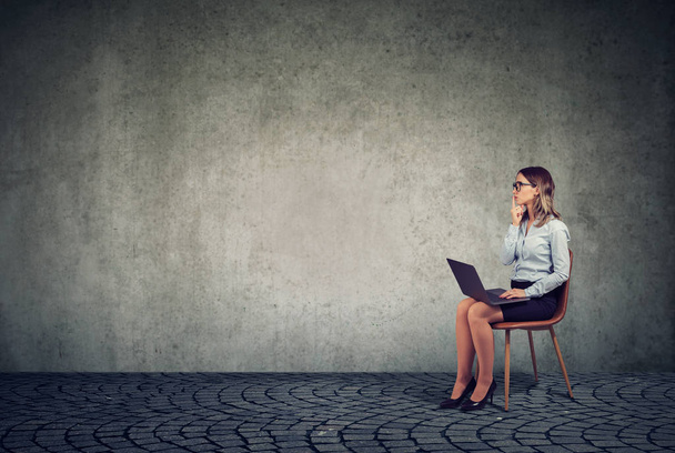 Przemyślane młoda kobieta w elegancki strój, siedząc na krześle z laptopem na kolanach i patrząc od burzy mózgów na pomysł - Zdjęcie, obraz