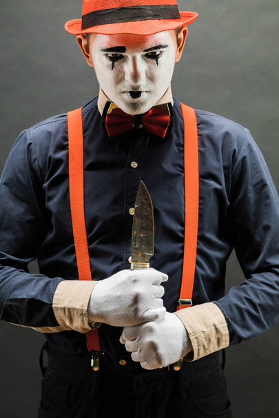 κλόουν και Απόκριες θέμα: τρελός κλόουν με μαχαίρι στο χέρι απομονωθεί σε σκοτεινό φόντο στο στούντιο - Φωτογραφία, εικόνα