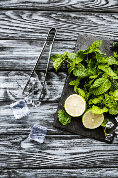 top view of ingredients for making mojito, ice cubes and tongs on wooden surface    - Фото, зображення