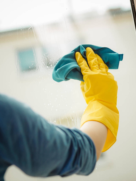 Weibliche Hand in gelben Handschuhen putzt Fenster mit blauem Lappen und Sprühwaschmittel. Frühjahrsputz, Hausaufgabenkonzept - Foto, Bild