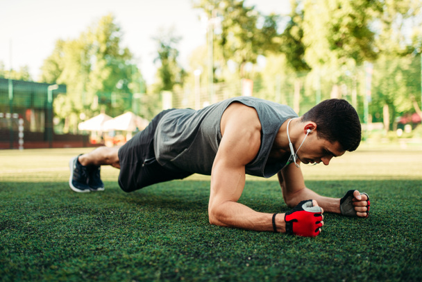Hombre atlético haciendo ejercicio push-up en un césped, entrenamiento de fitness al aire libre. Deportista muscular en el entrenamiento deportivo en el parque de verano
 - Foto, Imagen