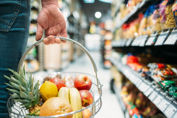 De hand van de mannelijke klanten met mandje met fruit, mensen kiezen van voeding in de supermarkt. Winkelen in de supermarkt - Foto, afbeelding