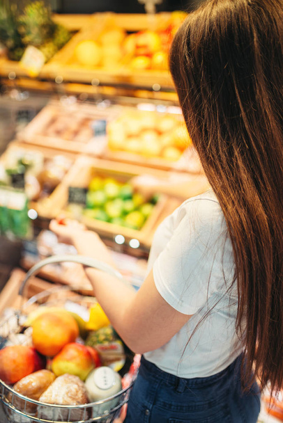 Женский клиент с корзиной против фруктовой секции в продовольственном магазине. Женщина в супермаркете
 - Фото, изображение