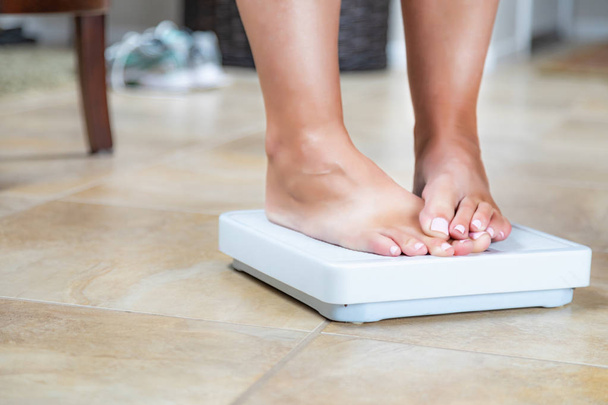 Mulher em pé na escala em casa cobrindo resultados de peso com dedos dos pés
. - Foto, Imagem