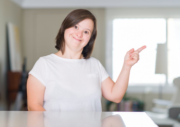 Женщина с синдромом Дауна дома очень счастлива, указывая рукой и пальцем в сторону.
 - Фото, изображение