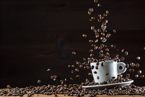 Arrangement of flying roasted dark coffee beans in white ceramic cup against black background - Photo, Image