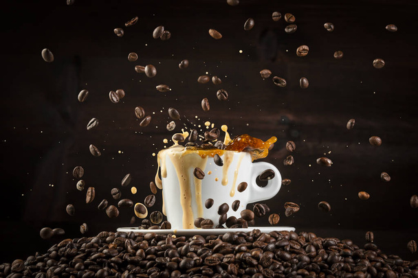 White ceramic cup of coffee with splashes and falling coffee beans on heap of grains against black background - Fotó, kép