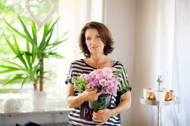 Beautiful middle age woman decorating home with flowers - Фото, изображение