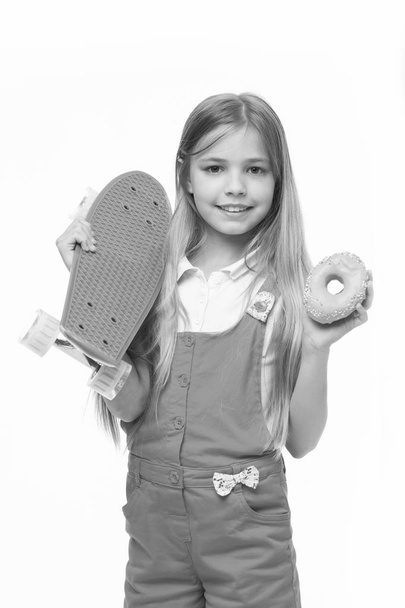 Little girl smile with skateboard and donut isolated on white. Child skater with doughnut and longboard. Skateboard kid with junk food. Sport and energy. Food for snack and dessert. dieting concept - Foto, imagen