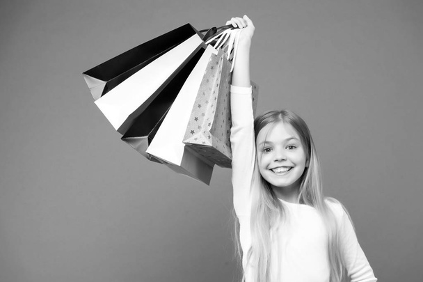 Щаслива дитина з паперовими мішками. Маленька дівчинка посміхається з сумками на фіолетовому фоні. Дитячий покупець на фіолетовому фоні. Святкова підготовка та святкування. Шопінг і продаж на чорну п'ятницю
 - Фото, зображення