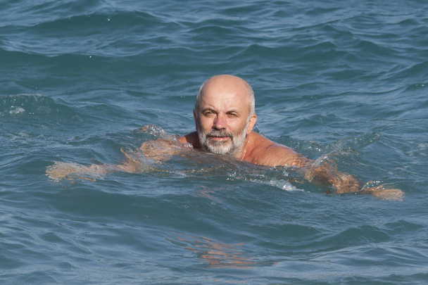 Bald man with a beard swims in the sea - Valokuva, kuva