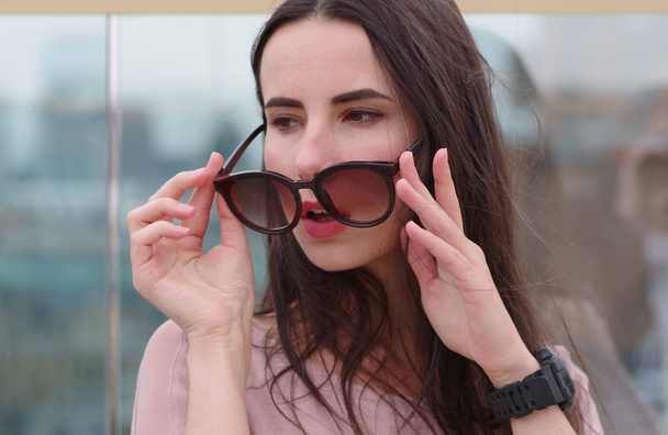 Długowłosy młoda kobieta brunetka bawi się okulary przeciwsłoneczne. - Zdjęcie, obraz