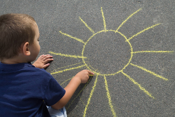 boy draws on the asphalt the sun with yellow chalk - Foto, immagini