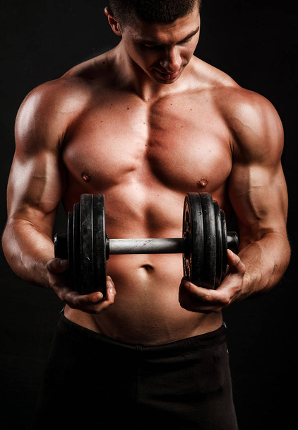 Muscular bodybuilder guy doing exercises with dumbbell over black background - Fotoğraf, Görsel