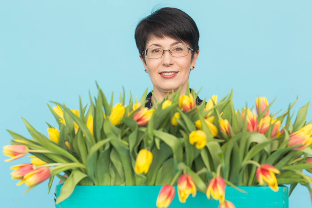 Bella donna caucasica di mezza età con un grande mazzo di tulipani su sfondo blu
 - Foto, immagini