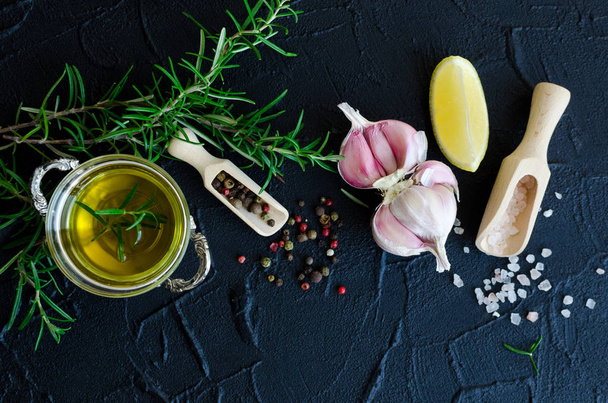 Herbs and spices selection - rosemary, garlic, lemon, salt, peppercorns and olive oil on dark stone table. Cooking ingredients concept. Food flat lay. Top view. - Photo, Image
