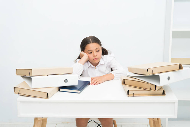 Too much to learn. Girl child tired exhausted sit at table near pile of books white background. Schoolgirl tired of studying and reading books. Kid school uniform tired face not want continue reading - Fotografie, Obrázek