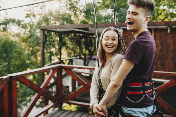Μερική άποψη του ευτυχισμένο ζευγάρι σε ειδικό εργαλείο με λουρί ασφάλειας που κρέμονται στο καλώδιο για zip line βόλτα στο πάρκο - Φωτογραφία, εικόνα