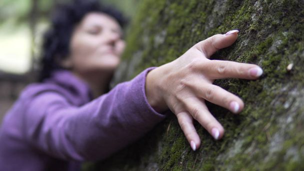 woman hugging large stone with moss in forest - Foto, afbeelding