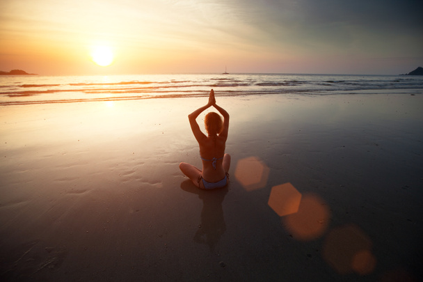 Deniz kıyısında oturan gün batımında yoga kadın - Fotoğraf, Görsel