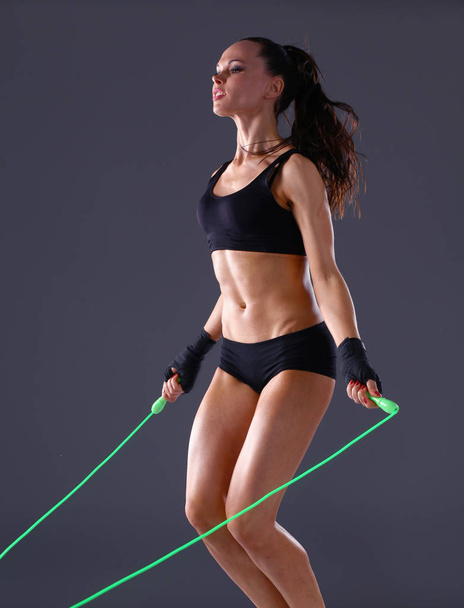 Muscular young woman standing on gray background. Muscular young woman. beautiful girl jumping rope - Foto, Imagen
