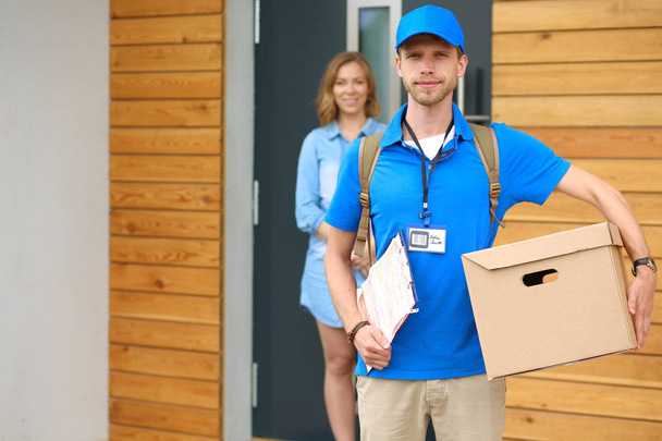 Smiling delivery man in blue uniform delivering parcel box to recipient - courier service concept. Smiling delivery man in blue uniform - Photo, image