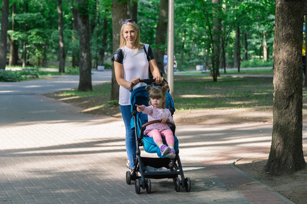 Περπάτημα ενώ σπρώχνει ένα καρότσι στο πάρκο μητέρας - Φωτογραφία, εικόνα