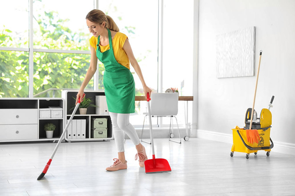 Young woman with broom and dustpan cleaning in office - 写真・画像