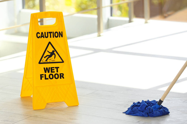 Señal de seguridad con frase Precaución suelo mojado y fregona, en interiores. Servicio de limpieza
 - Foto, imagen