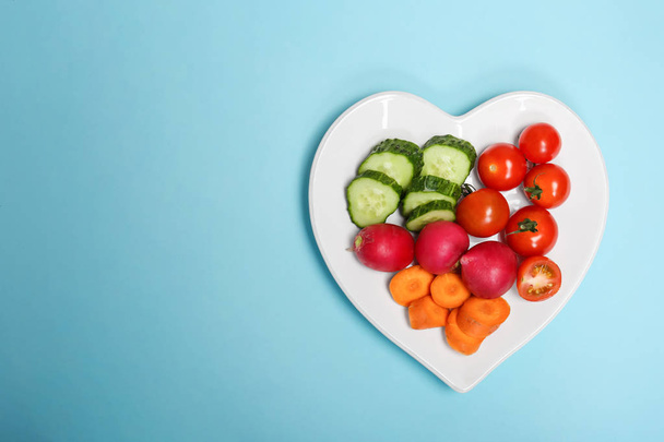 Heart shaped plate with fresh vegetables on color background, top view. Cardiac diet - Foto, imagen