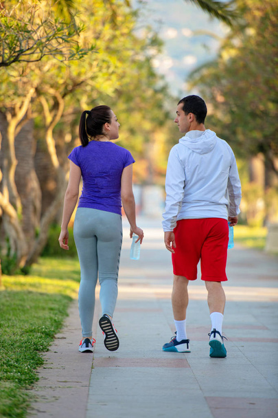 νέος σπορ άνδρα και γυναίκας σε αθλητικά περπάτημα στο σοκάκι μετά από τρέξιμο, πίσω όψη  - Φωτογραφία, εικόνα