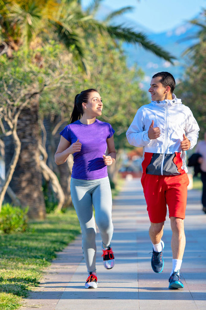 young smiling sporty man and woman in sportswear jogging along palm trees - Photo, Image