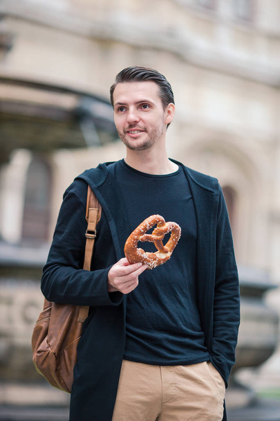 Beautiful young man eating pretzel outdoors in Europe - Photo, Image